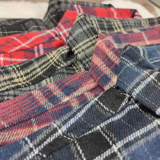 Zestawienie różnych kolorów męskich koszul flanelowych w kratę ułożonych w stos.