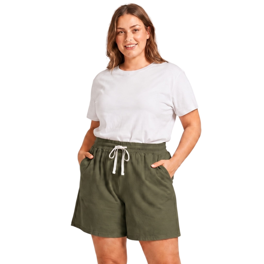 Modelka plus size trzyma dłonie w kieszeniach oliwkowych szortów damskich bawełnianych, tło białe.