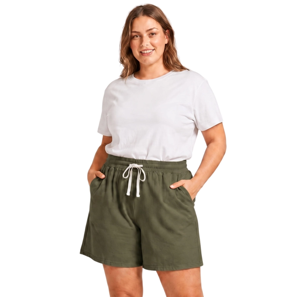 Modelka plus size trzyma dłonie w kieszeniach oliwkowych szortów damskich bawełnianych, tło białe.